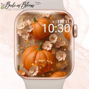 Puede incluir: Un reloj inteligente con marco de color claro y pantalla digital que muestra la hora 10:30 y la fecha FRI 11. La pantalla presenta un gráfico de calabazas naranjas, flores claras y pequeños detalles dorados sobre un fondo de color beige.