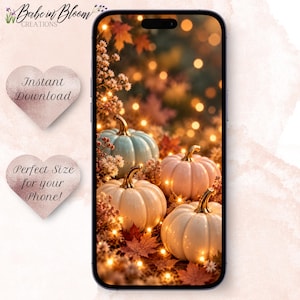 Puede incluir: Un teléfono inteligente que muestra un fondo de pantalla digital con cuatro calabazas en tonos azul pálido, crema y blanco, rodeadas de hojas de otoño y luces cálidas. La pantalla presenta una escena estacional con una iluminación bokeh suave.