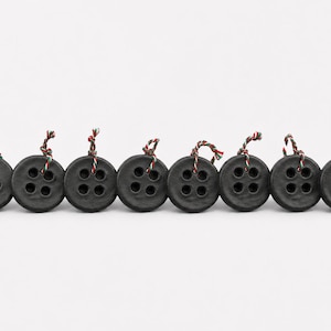 May include: A row of eight circular black buttons, each featuring four central holes. Each button has a small piece of twisted red, white, and green cord tied through the top holes, creating a consistent decorative detail across the set.