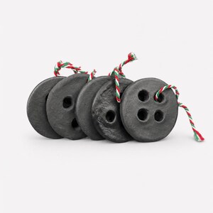 May include: A set of five circular black buttons with a textured, matte finish. Each button features four holes and is threaded with a piece of red, white, and green twisted string. The buttons are arranged in a slightly overlapping horizontal row.