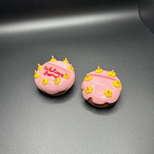 May include: Two pink frosted cakes with yellow flower decorations. One cake says "Welcome Home" in red lettering.