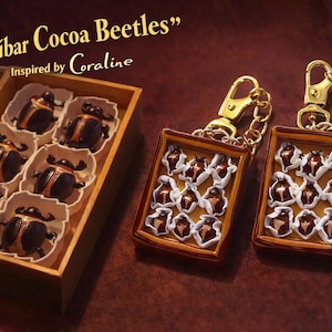 Puede incluir: Una caja de madera con seis figuras de escarabajos marr&oacute;n oscuro en moldes de papel blanco, junto a dos llaveros rectangulares con dise&ntilde;os de escarabajos en miniatura en blanco y marr&oacute;n, con el texto Zanzibar Cocoa Beetles Inspired by Coraline.