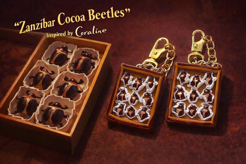 Puede incluir: Una caja de madera con seis figuras de escarabajos marr&oacute;n oscuro en moldes de papel blanco, junto a dos llaveros rectangulares con dise&ntilde;os de escarabajos en miniatura en blanco y marr&oacute;n, con el texto Zanzibar Cocoa Beetles Inspired by Coraline.