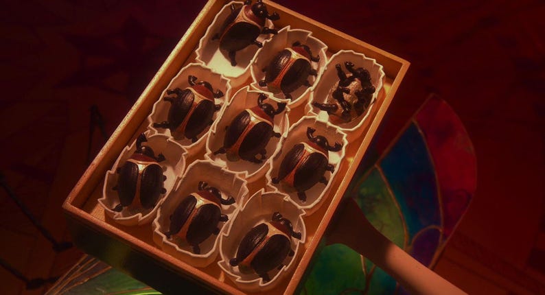 Puede incluir: Una caja rectangular de madera que contiene nueve compartimentos individuales, cada uno con una peque&ntilde;a figura de escarabajo. Los escarabajos son negros con cubiertas alares de color bronce met&aacute;lico y cuernos curvos, dispuestos en cuadr&iacute;cula.