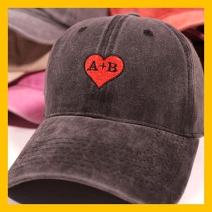May include: A black denim baseball cap with a red heart embroidered on the front. The heart has the text "A+B" inside.