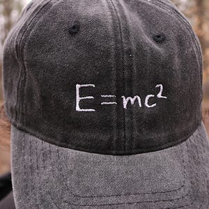 May include: A black denim baseball cap with white embroidery of the equation "E=mc2".