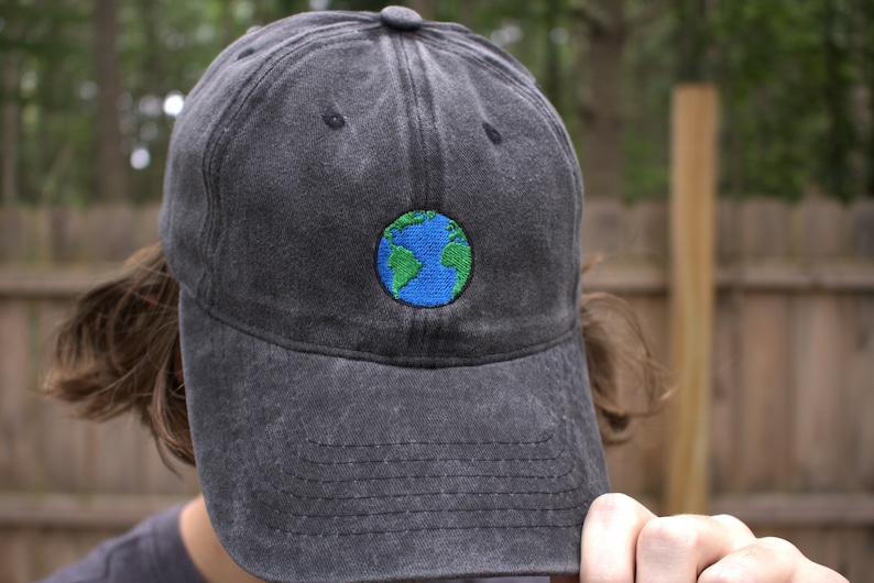 Puede incluir: Una gorra de b&eacute;isbol negra con un globo terr&aacute;queo bordado en azul y verde en la parte delantera.