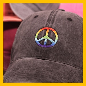 May include: A black denim baseball cap with a rainbow peace sign embroidered on the front.