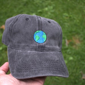 Puede incluir: Una gorra de b&eacute;isbol negra con una peque&ntilde;a imagen bordada de un globo terr&aacute;queo azul y verde.