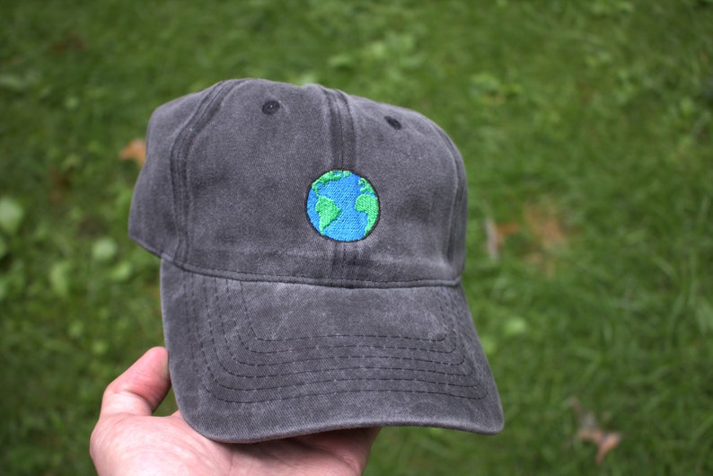 Puede incluir: Una gorra de b&eacute;isbol negra con una peque&ntilde;a imagen bordada de un globo terr&aacute;queo azul y verde.