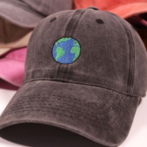 Puede incluir: Una gorra de b&eacute;isbol de algod&oacute;n negro, desgastada, con un dise&ntilde;o de globo terr&aacute;queo bordado en verde y azul.