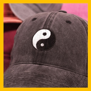 Op de afbeelding: Een zwarte baseballpet met een wit yin-yang symbool geborduurd op de voorkant.