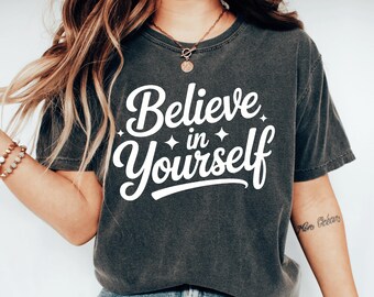 May include: Dark grey t-shirt featuring the white text "Believe in Yourself", with star accents. The casual tee is suitable for everyday wear. The shirt is a relaxed fit.