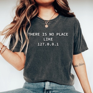 Könnte beinhalten: Dunkelgraues T-Shirt mit dem weißen Text "THERE IS NO PLACE LIKE 127.0.0.1". Das T-Shirt hat einen Vintage-Look. Ein lässiges Kleidungsstück.