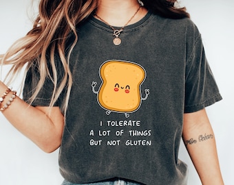 May include: A dark gray t-shirt with a cartoon image of a slice of bread with a smiling face. The text "I tolerate a lot of things but not gluten" is printed below the image.