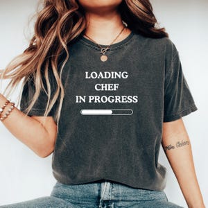 May include: A dark gray t-shirt with the text "LOADING CHEF IN PROGRESS" and a progress bar graphic printed in white.