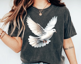 Könnte beinhalten: Dunkelgraues T-Shirt mit einer detaillierten Illustration einer weißen Taube im Flug. Die Taube hat ausgebreitete Flügel. Das T-Shirt ist ein lässiger Stil, geeignet für den Alltag.