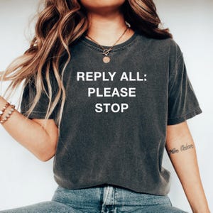 以下が含まれることがあります： 白地に「REPLY ALL: PLEASE STOP」とプリントされた濃いグレーのTシャツ