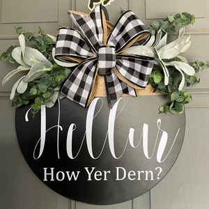 Könnte beinhalten: Schwarz-weiß kariertes Band mit Juteband und Grün auf einem schwarzen runden Holzschild mit dem Text "Hello How Yer Dern?"