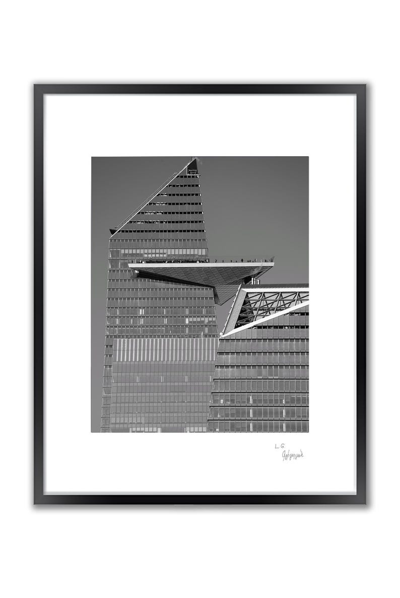 A framed black and white photo shows a modern building with a triangular roof and a large, flat observation deck.