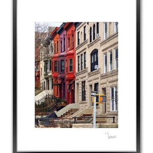 A framed color photo shows a row of brownstone buildings with varying colors, including red and orange, under a blue sky.