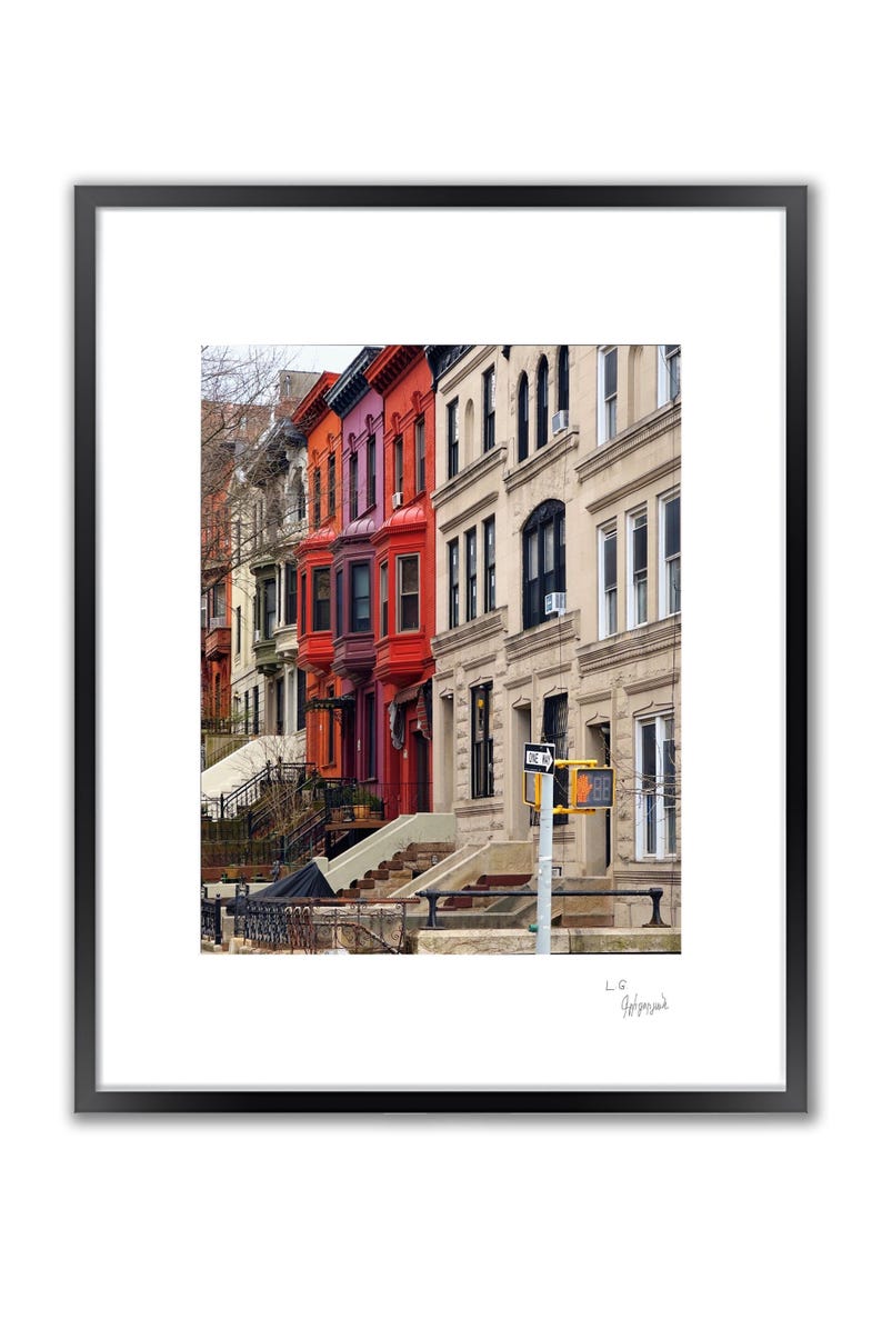 A framed color photo shows a row of brownstone buildings with varying colors, including red and orange, under a blue sky.