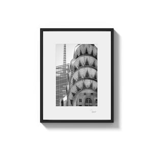 A framed black and white photo shows the top of a building with a rounded, tiered, and textured roof, with a signature in the bottom right corner.