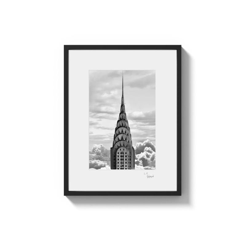 A framed black and white photo shows the spire of a tall, ornate building rising above clouds.