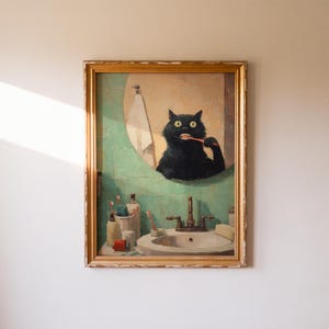 K&ouml;nnte beinhalten: Ein gerahmtes Gem&auml;lde zeigt eine schwarze Katze, die sich in einem Badezimmerspiegel die Z&auml;hne putzt. Die Katze befindet sich vor einer gr&uuml;n gefliesten Wand, mit einem Waschbecken und Toilettenartikeln. Das Gem&auml;lde hat einen goldenen Rahmen und h&auml;ngt an einer wei&szlig;en Wand.