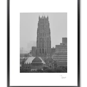 A framed black and white photo shows a tall, gothic-style building with a pointed roof, surrounded by other buildings.
