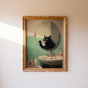 K&ouml;nnte beinhalten: Gerahmtes Kunstwerk, das eine schwarze Katze zeigt, die sich in einem Badezimmerspiegel die Z&auml;hne putzt. Die Katze spiegelt sich in einem runden Spiegel &uuml;ber einem Vintage-Waschbecken. Das Badezimmer hat eine gr&uuml;n geflieste Wand und einen goldfarbenen Rahmen.