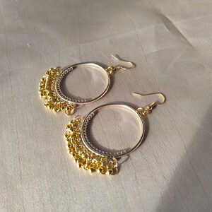Op de afbeelding: Een paar gouden creolen met een hangende ketting van kleine gouden kralen.