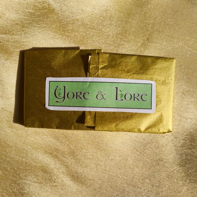 Op de afbeelding: Een goudkleurig tissuepapierpakket met een wit label waarop in groene letters "Yore & Lore" staat.