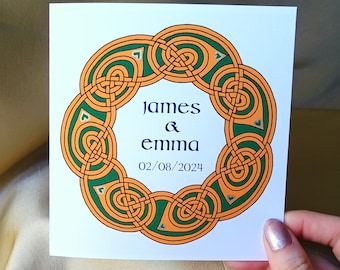 May include: A white card featuring a Celtic knot design in orange and green. The card reads "james & emma" and "02/08/2024" in navy blue text.