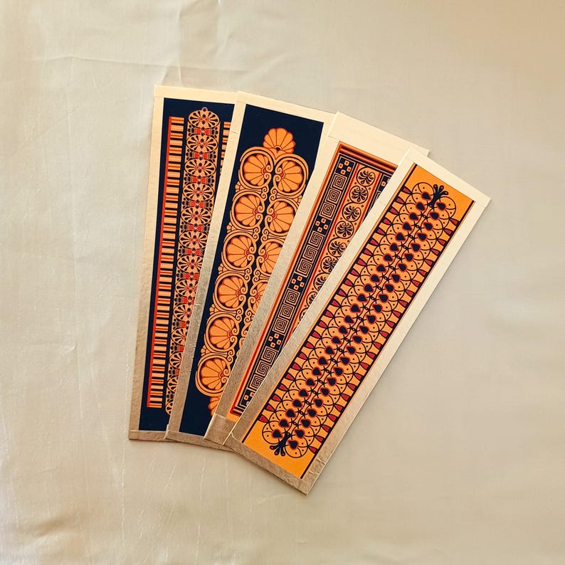 May include: Four decorative bookmarks featuring intricate geometric patterns in orange, black and white on a gold background.