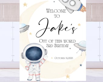 May include: A rectangular birthday welcome sign featuring a watercolor astronaut, a rocket ship, and two flying saucers against a crescent moon background. The text reads: Welcome to Jake's Out of This World 3rd Birthday, October 14, 2023.