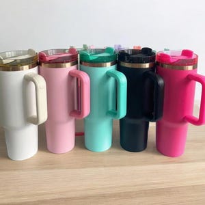 May include: Six stainless steel travel mugs with handles. The mugs are in various colors: white, pink, turquoise, black, and hot pink. Each mug has a lid with a straw hole.