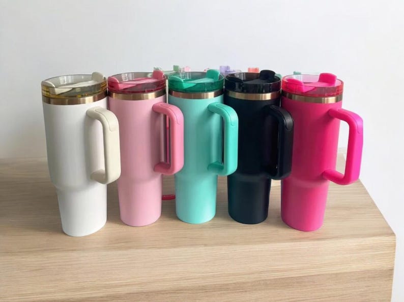 May include: Six stainless steel travel mugs with handles. The mugs are in various colors: white, pink, turquoise, black, and hot pink. Each mug has a lid with a straw hole.