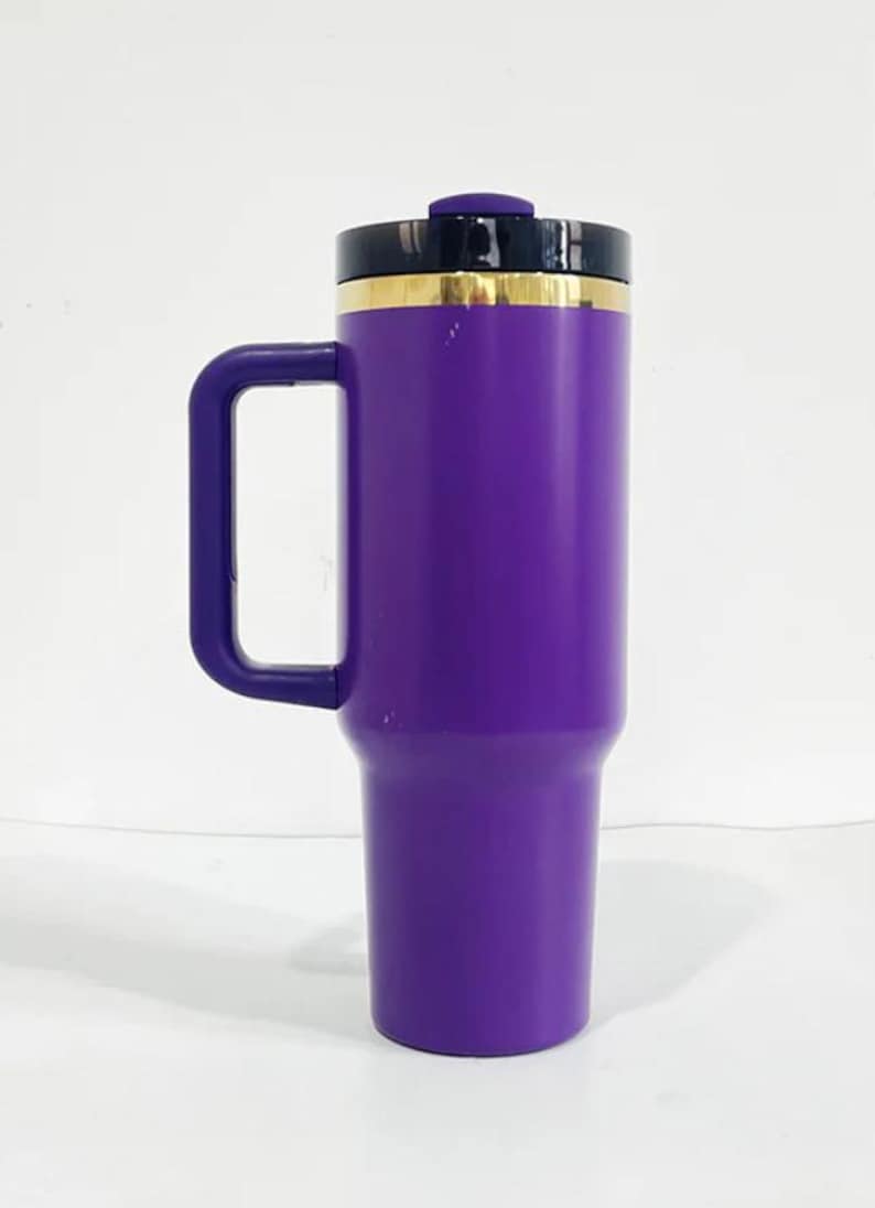 May include: A purple travel mug with a black lid and a gold band around the top. The mug has a handle and is made of stainless steel.