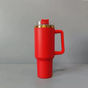 May include: A red stainless steel travel mug with a gold rim and a handle. The mug has a clear lid with a red slider.