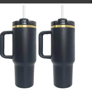 May include: Two black stainless steel travel mugs with gold accents and lids. Each mug has a handle and a clear straw.