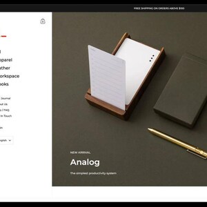 Könnte beinhalten: Ein Screenshot einer Website, der einen dunkelgrauen Hintergrund mit einem rot-weißen Logo zeigt, auf dem "Kingdom" steht. Die Website ist für ein Thema namens "Analog" und zeigt eine dunkelgrüne Box mit einem weißen Etikett, auf dem "Analog" steht. Die Website zeigt auch einen Screenshot eines Mobiltelefons, auf dem eine Website mit einem rot-weißen Logo zu sehen ist, auf dem "k_" steht, und dem Text "Basic T-shirts".