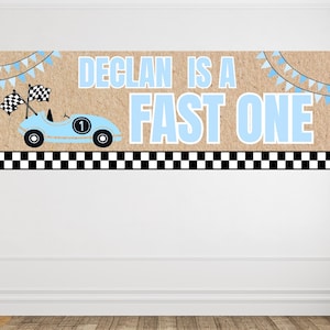 Könnte beinhalten: Ein rechteckiges Banner mit beigem, strukturiertem Hintergrund und dem hellblauen Text DECLAN IS A FAST ONE. Das Design zeigt einen hellblauen Rennwagen mit der Nummer 1, zwei Zielflaggen, hellblaue Wimpel und eine schwarz-weiß karierte Bordüre.