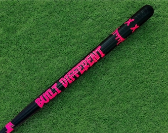 May include: Black baseball bat with the words "BUILT DIFFERENT" in bright pink lettering. The bat also has pink accents and two pink "XX" marks near the top. The bat is set against a green background.