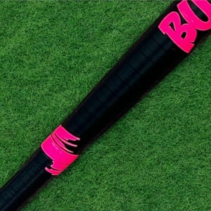 Puede incluir: Bate de b&eacute;isbol negro con detalles rosas y la palabra "BULL" en rosa. El bate se encuentra sobre un fondo verde, lo que sugiere un tema deportivo. El dise&ntilde;o del bate incluye un &aacute;rea de agarre texturizada.