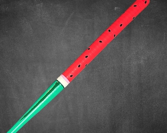 May include: A watermelon-themed baseball bat. The top portion is red with black seed-shaped cutouts, and the handle is green. A white and pink band separates the red and green sections. The bat is set against a dark gray background.