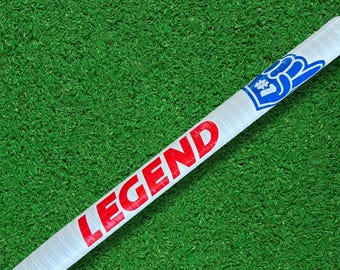 May include: A white foam finger with the word "LEGEND" in red block letters. The end of the foam finger has a blue hand graphic and the number 1. The foam finger is on a green surface.