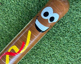 May include: Brown inflatable baseball bat with a smiling face and colorful accents. The bat features a cartoon-style design with a white smile, black eyes, and yellow and red stripes.
