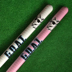May include: Two cylindrical objects, one white and one pink, with the word "GOAT" printed in black and light blue. Each has a graphic of a goat wearing sunglasses. The background is green.