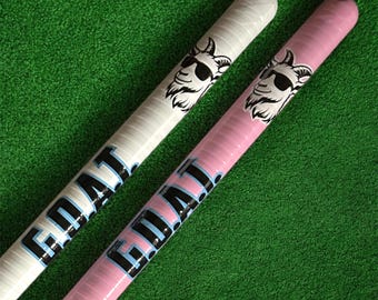 May include: Two cylindrical objects, one white and one pink, with the word "GOAT" printed in black and light blue. Each has a graphic of a goat wearing sunglasses. The background is green.